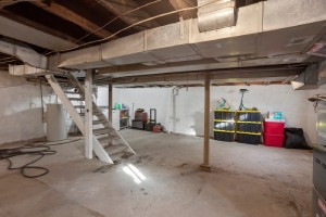 An unfinished basement with a staircase, storage shelves and a washer and dryer