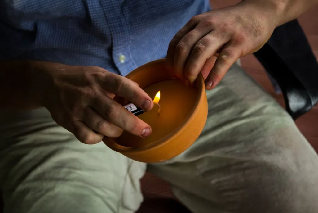 Person using a lighter to light a potted citronella candle to keep mosquitoes away.