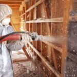 A worker blowing pest control insulation into an open wall.