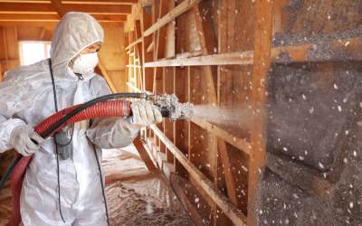 A worker blowing pest control insulation into an open wall.
