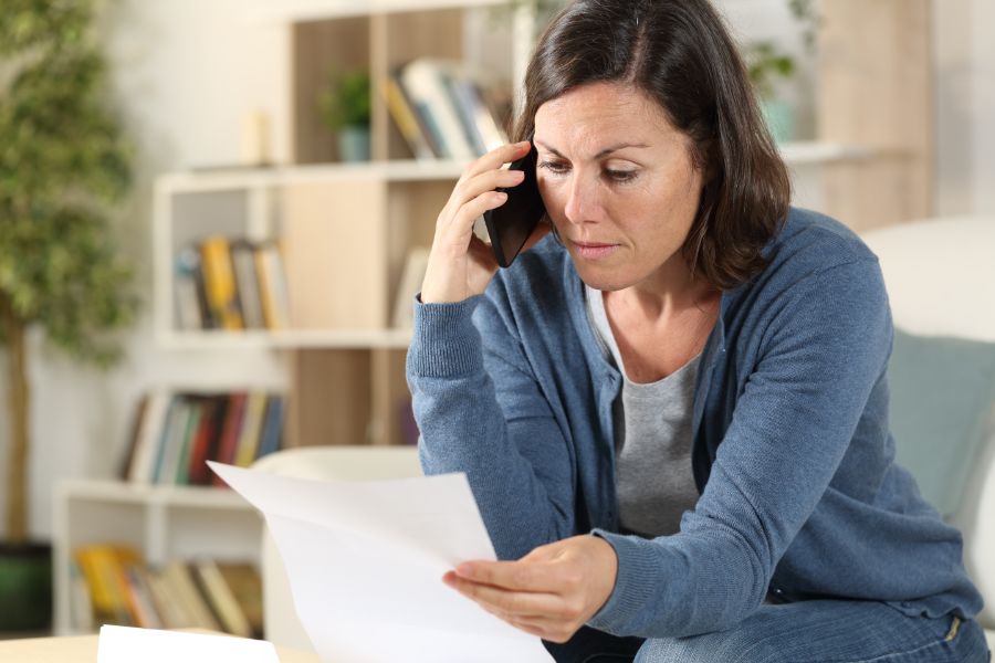 Woman on the phone holding and looking at a piece of paper.